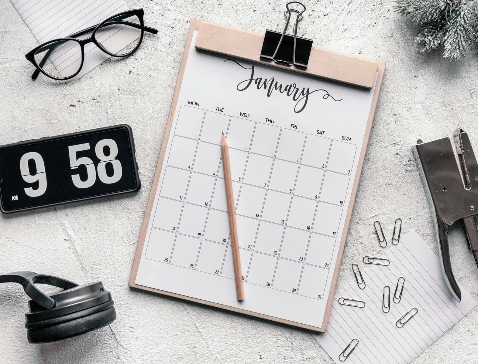 Calendario de papel sobre un portapapeles, con un lápiz, un reloj y material de escritorio