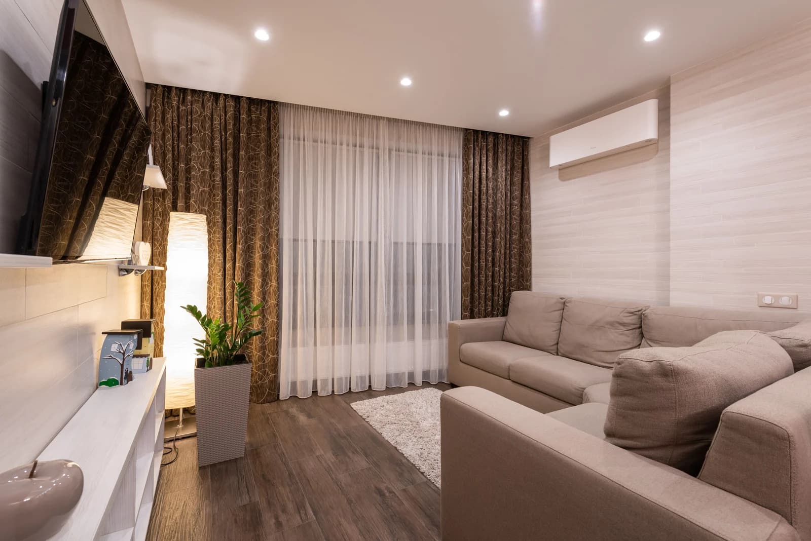 Salón con sofá en esquina, cortinas y suelo de madera