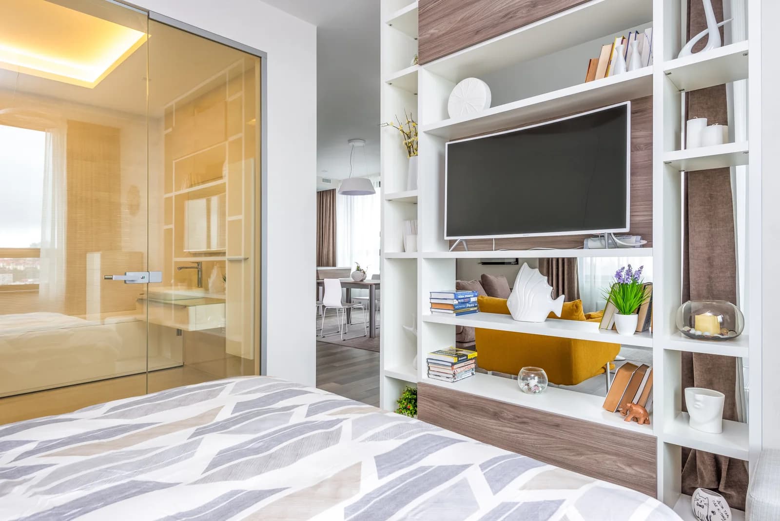 Cama en primer plano, estanterías y una zona de comedor al fondo.