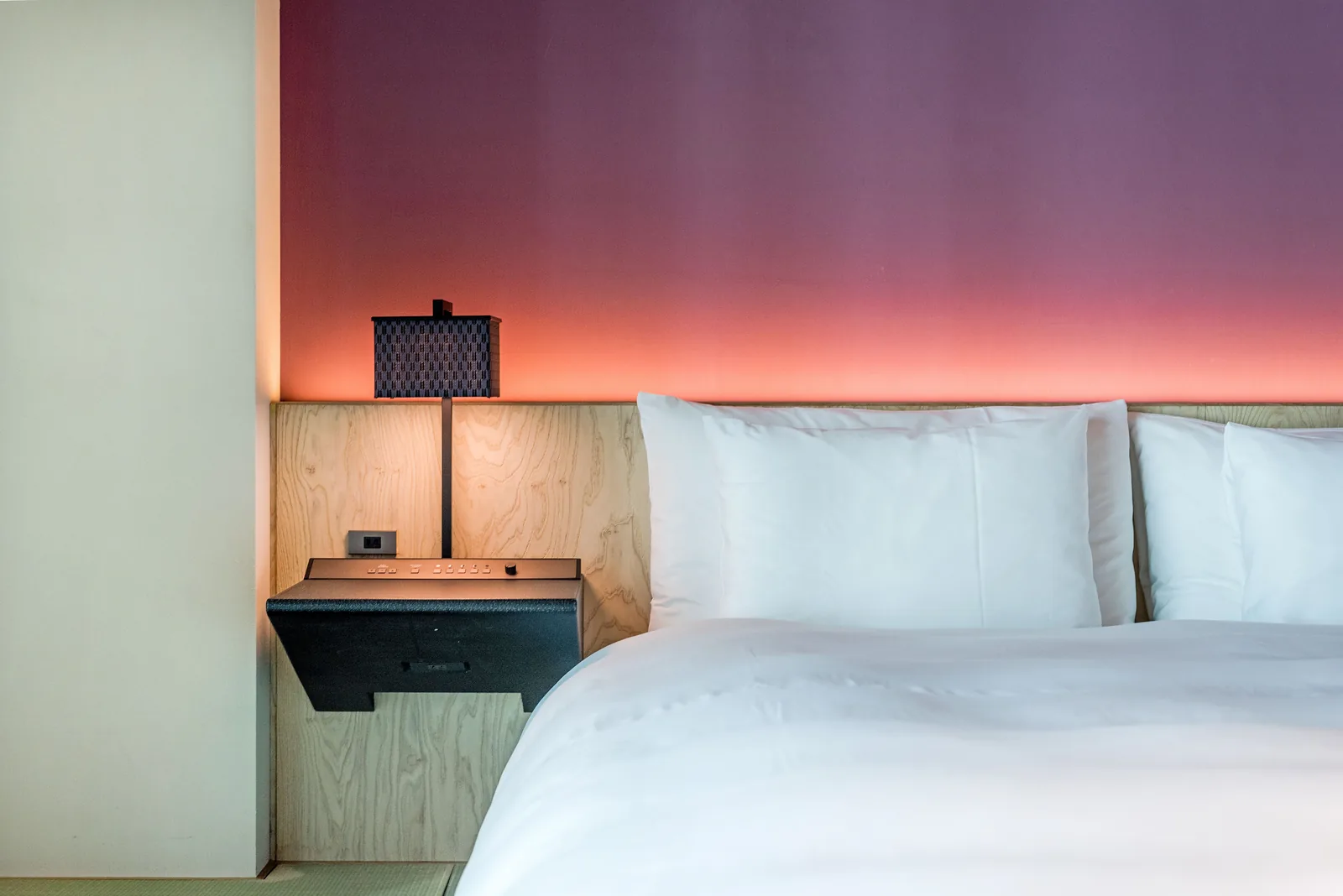 Cama hecha con almohadas blancas junto a un cabecero de madera y una lámpara.
