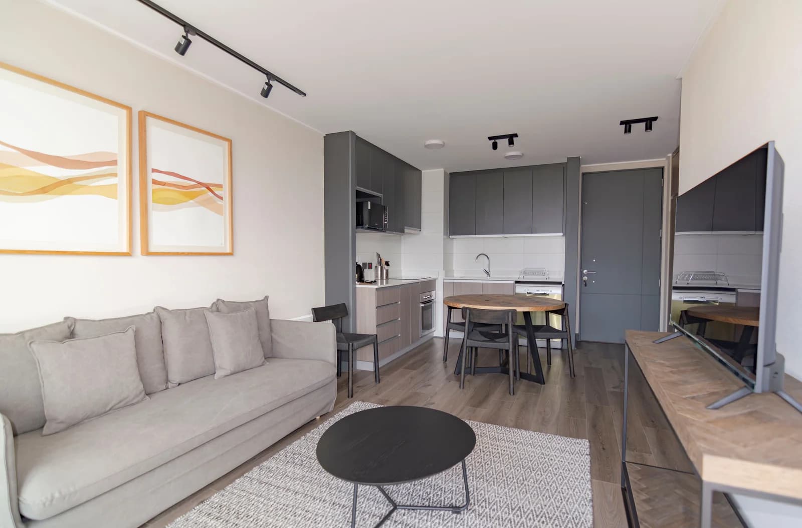 Salón con sofá gris, mesa de comedor y cocina abierta al fondo.