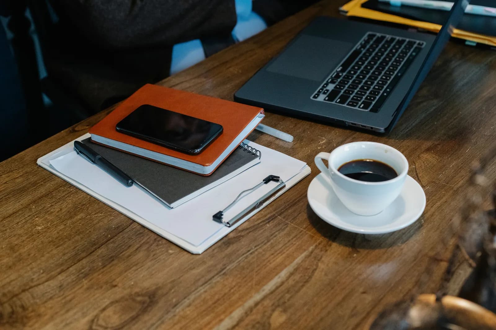 Portátil, cuadernos, móvil y una taza de café sobre una mesa de madera.